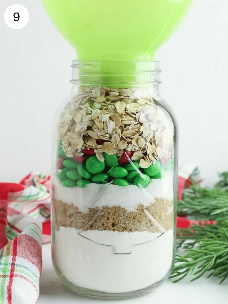 ingredients for oatmeal cookies in mason jar with green funnel.
