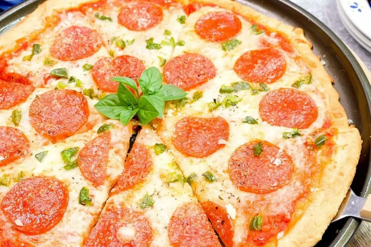 pizza sliced and being served with pepperoni and fresh basil.